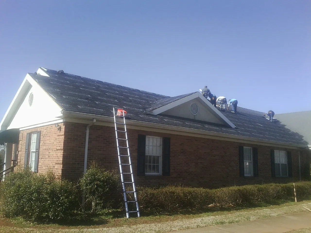 Crew tearing shingles off a brick ranch roof with a ladder set — Emergency Roof Repair work by our crew in Highland Park