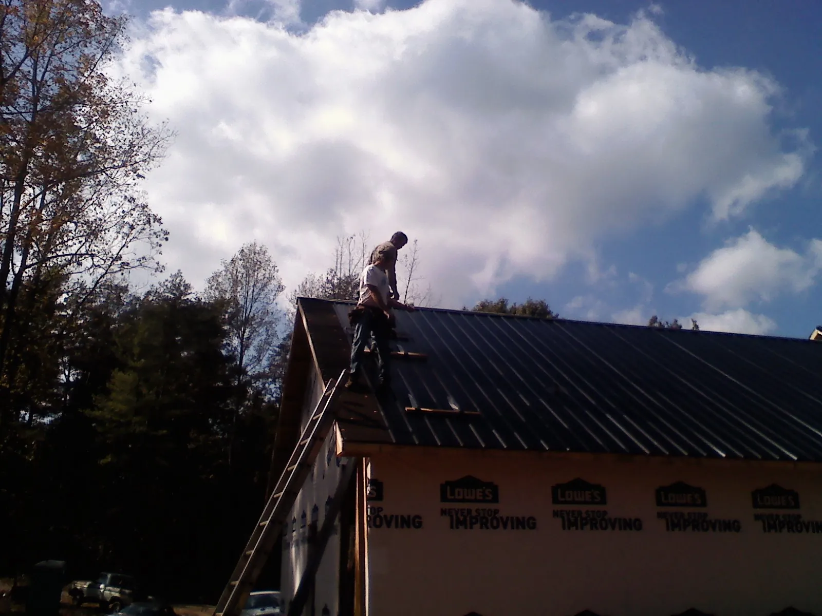Roofer fastening dark metal panels high against a cloudy sky, from a Roof Inspection job in Highland Park